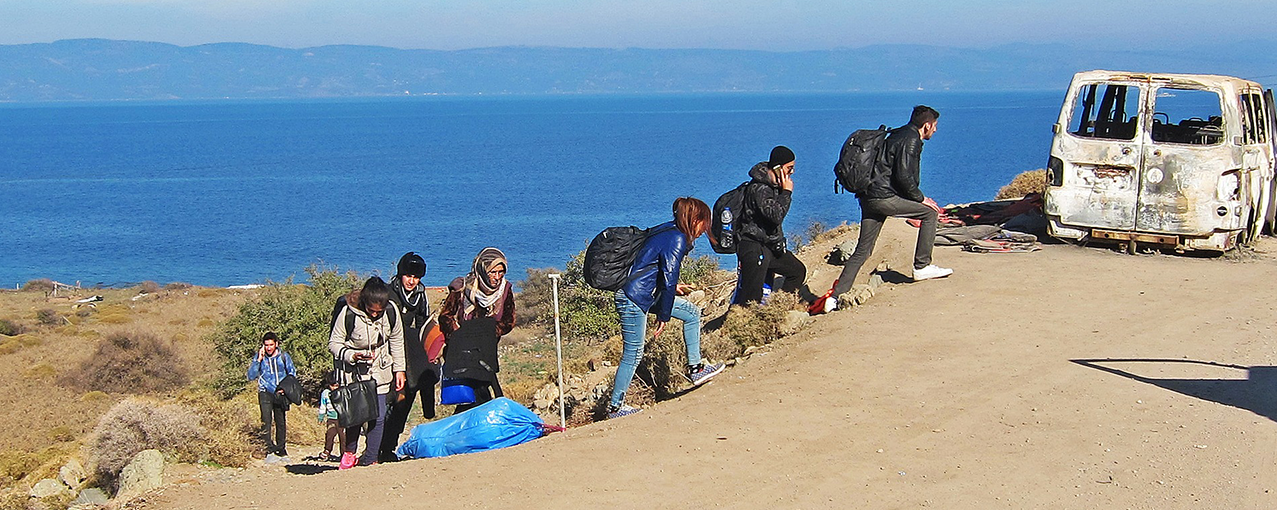 A imagem mostra oito pessoas subindo um morro em direção a uma estrada de terra. Aparecem, ainda, mar, céu e a carcaça de um carro